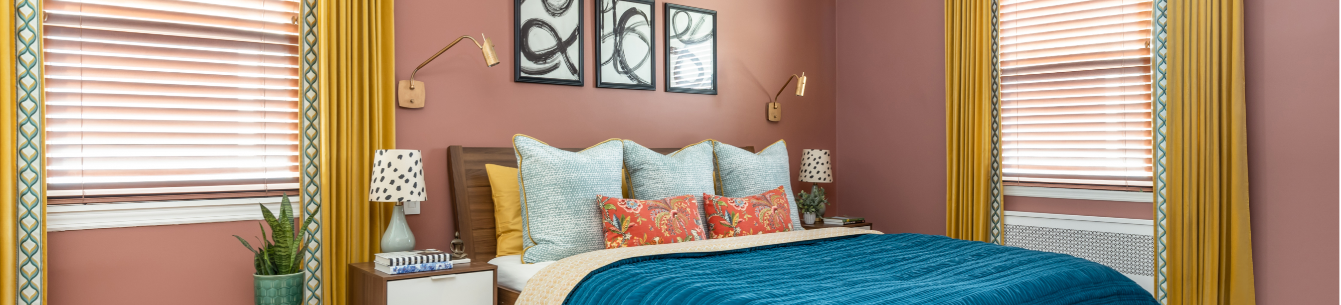 Primary bedroom with red walls, yellow drapes, area rug with abstract colorful pattern, wooden floors and blue bed cover