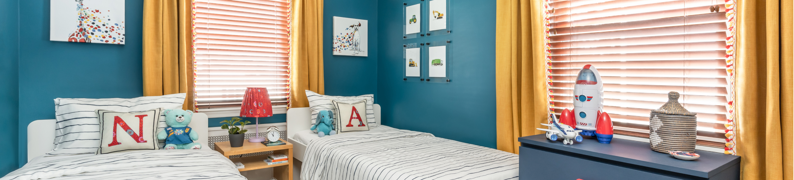 Kids’ bedroom with twin beds, dark blue walls, yellow drapes, and area rug with geometric design