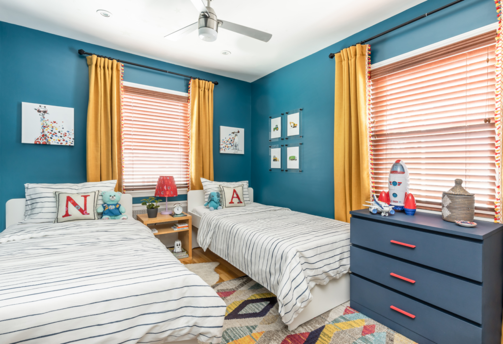 Kids’ bedroom with twin beds, dark blue walls, yellow drapes, and area rug with geometric design ALT Text: