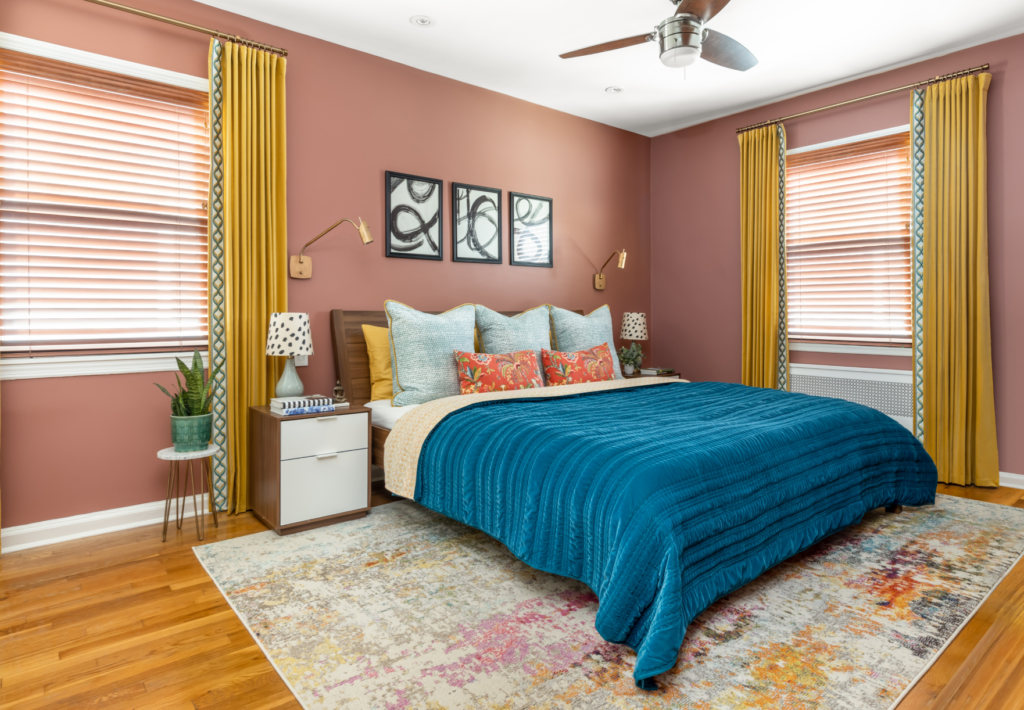 Master bedroom with light red walls, yellow drapes, wooden floors and blue bed sheet